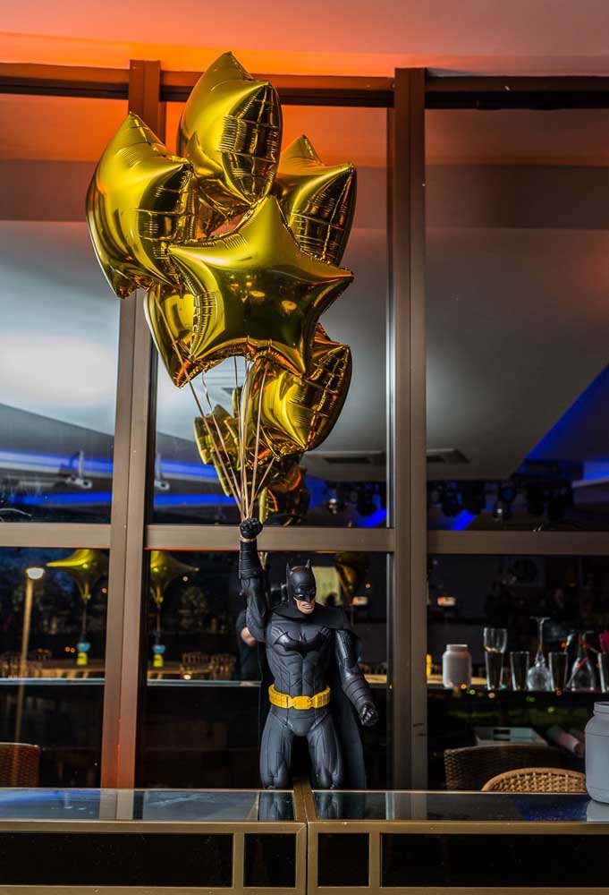 Vamos colocar o Batman para animar a festa? Pendure alguns balões metálicos no braço do boneco.